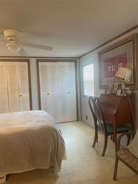 A bedroom features a bed, louvered closet doors, a wooden desk, and a ceiling fan — 501 OAK RIDGE E, LAKELAND, FL
