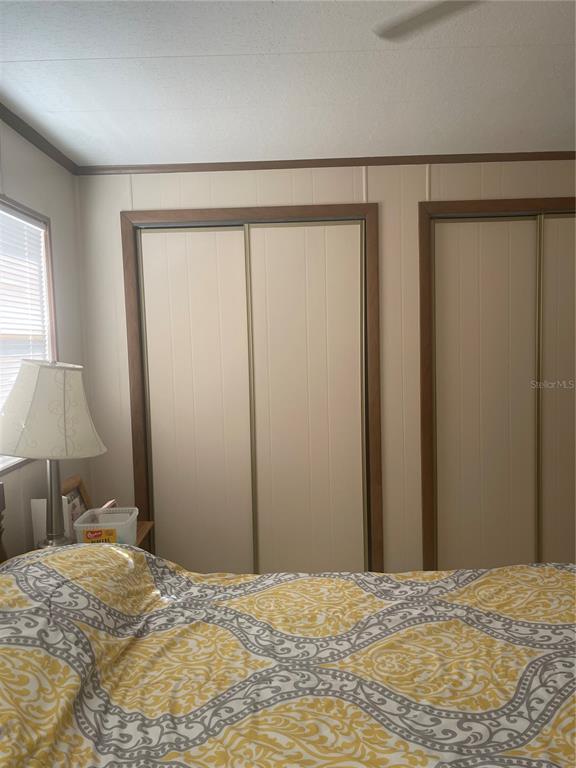 A bedroom features a bed with a yellow patterned comforter and two sets of closet doors — 501 OAK RIDGE E, LAKELAND, FL