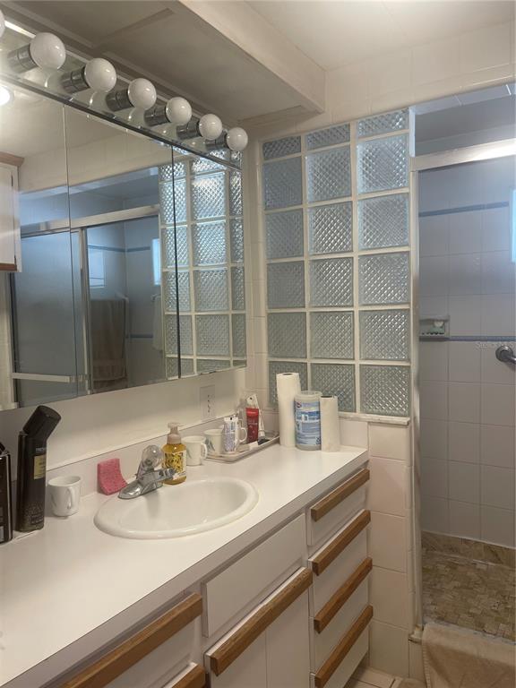 A bathroom vanity with a white countertop, glass block wall, and a walk-in shower — 501 OAK RIDGE E, LAKELAND, FL