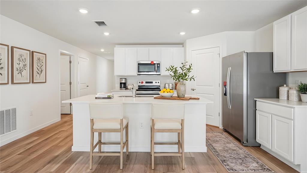 A modern kitchen features white cabinets, a central island with two stools, and stainless appliances — 4596 KONA CIRCLE, SPRING HILL, FL
