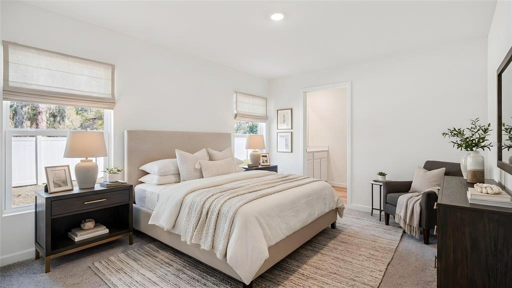 A bright bedroom features a neutral-toned bed, two nightstands, a gray armchair, and two windows — 4596 KONA CIRCLE, SPRING HILL, FL