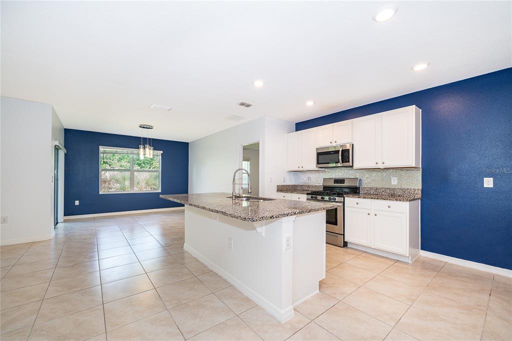 A kitchen with white cabinets, granite countertops, a central island, and blue accent walls — 239 LAZIO CIRCLE, DEBARY, FL