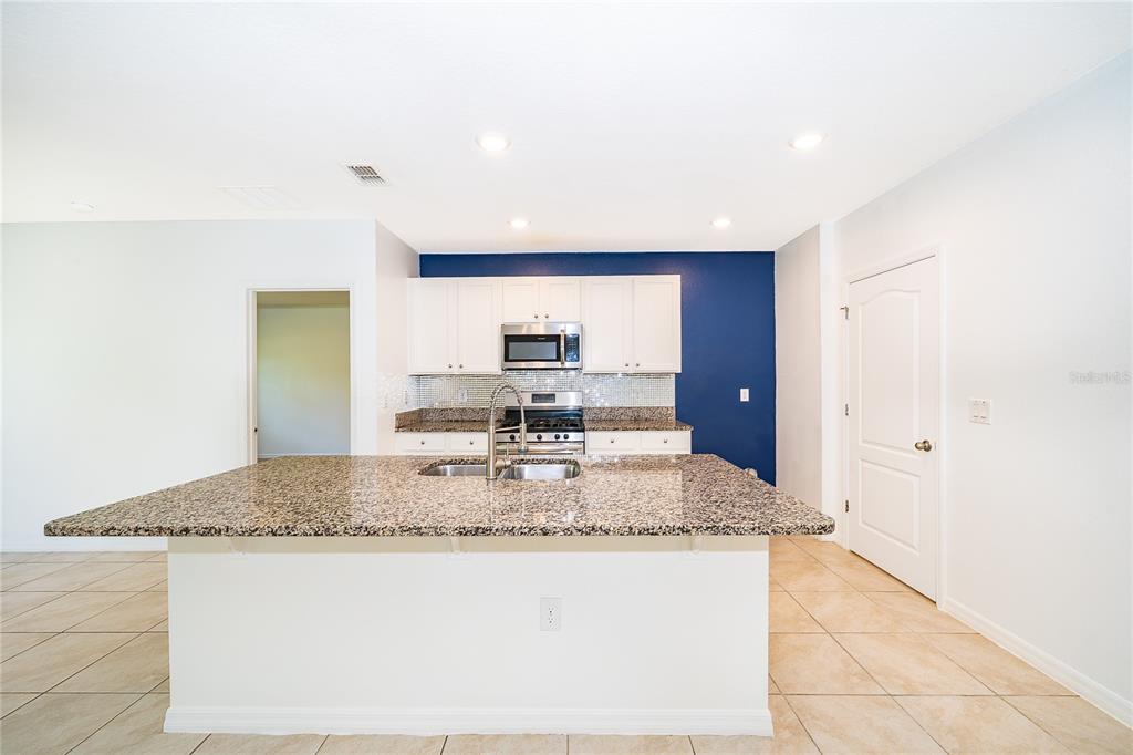 A kitchen features a granite-topped island, white cabinets, stainless steel appliances, and a blue wall — 239 LAZIO CIRCLE, DEBARY, FL