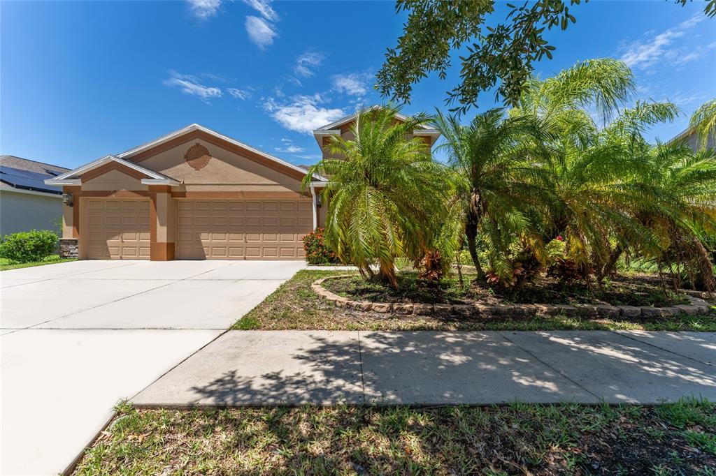 A tan suburban house with a three-car garage and palm trees in the front yard — 2637 YUKON CLIFF DRIVE, RUSKIN, FL