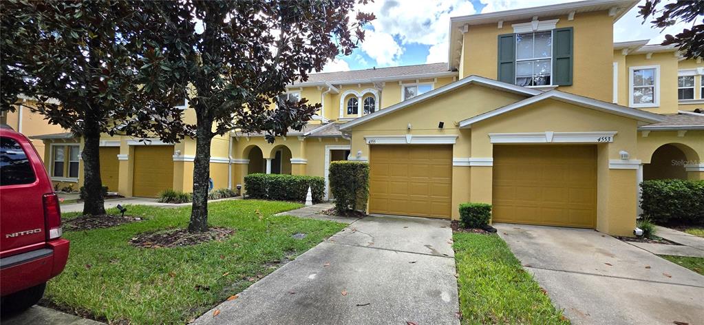 A yellow two-story townhouse exterior features two garage doors and a concrete driveway — 4555 LIMERICK DRIVE, TAMPA, FL