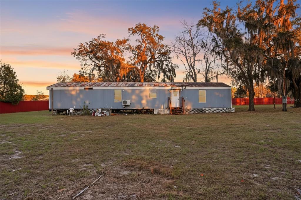 A single-story mobile home sits on a large, grassy lot with mature trees at sunset — 18441 RIGSBY ROAD, SPRING HILL, FL