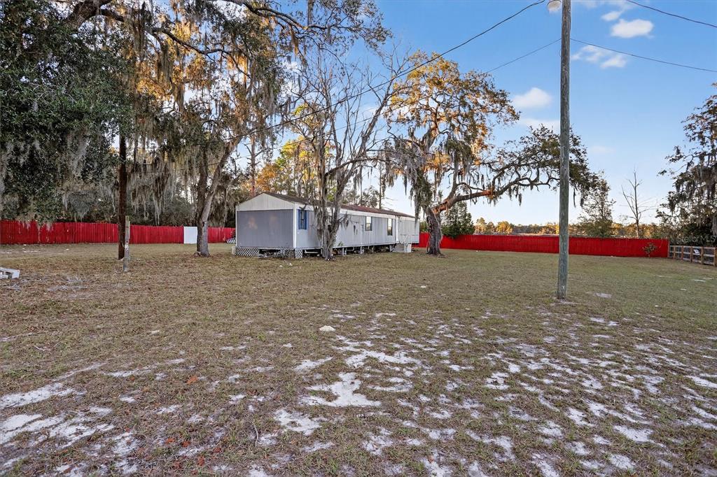 A mobile home sits on a large, grassy lot enclosed by a red wooden fence — 18441 RIGSBY ROAD, SPRING HILL, FL