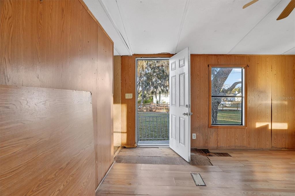 An interior room features wood-paneled walls, light-colored flooring, and an open door leading outside — 18441 RIGSBY ROAD, SPRING HILL, FL