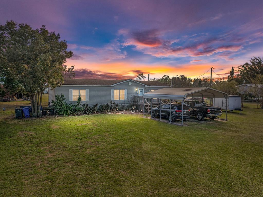 A single-story house with a metal carport and two parked vehicles under a sunset sky — 11404 LITHIA PINECREST ROAD, LITHIA, FL