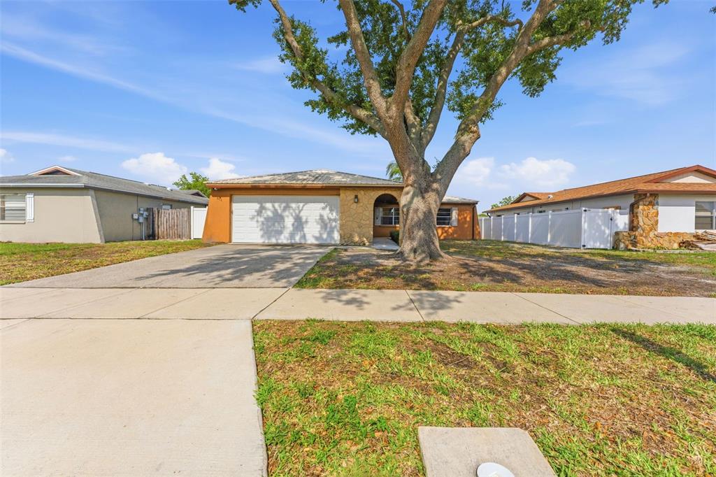 A single-story house with a two-car garage, stone facade, and a large tree in front — 611 TANGERINE DRIVE, OLDSMAR, FL
