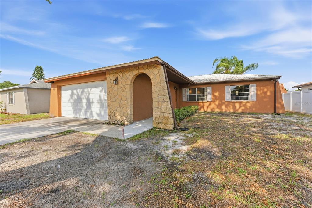 A single-story house with a stone-accented entryway, a two-car garage, and a sandy front yard — 611 TANGERINE DRIVE, OLDSMAR, FL