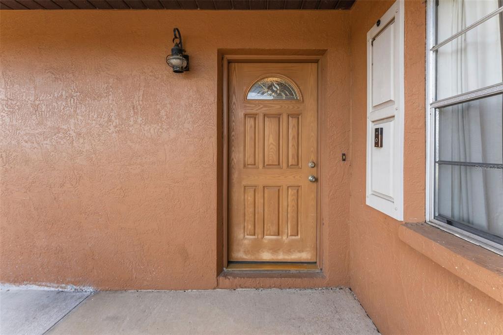 A wooden front door with a glass insert is set into a textured orange exterior wall — 611 TANGERINE DRIVE, OLDSMAR, FL