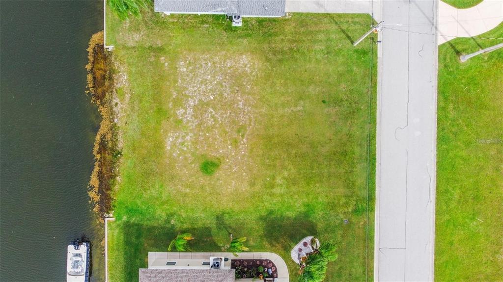 An aerial view shows a vacant, grassy waterfront lot situated between two residential properties — 4009 CROAKER DRIVE, HERNANDO BEACH, FL