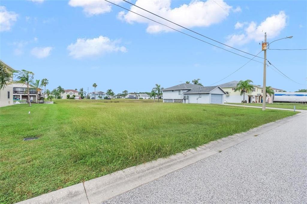 A vacant, grassy residential lot sits next to a house under a blue sky — 4009 CROAKER DRIVE, HERNANDO BEACH, FL