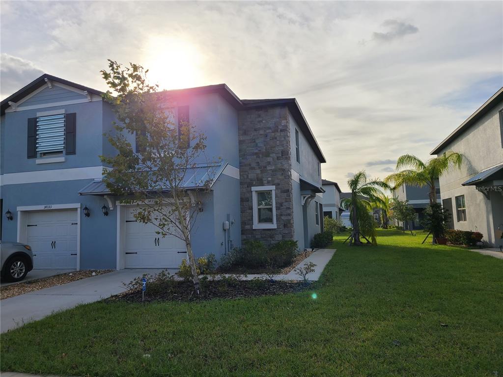A two-story blue townhouse with a stone facade, a two-car garage, and a grassy yard — 14331 EASY GOER STREET, RUSKIN, FL