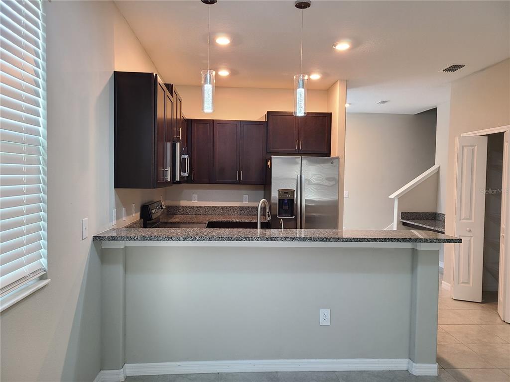 A kitchen features dark wood cabinets, granite countertops, stainless steel appliances, and a breakfast bar — 14331 EASY GOER STREET, RUSKIN, FL