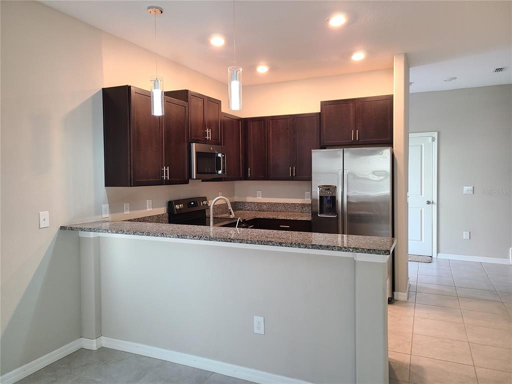 A kitchen features dark wood cabinets, granite countertops, stainless steel appliances, and a breakfast bar — 14331 EASY GOER STREET, RUSKIN, FL