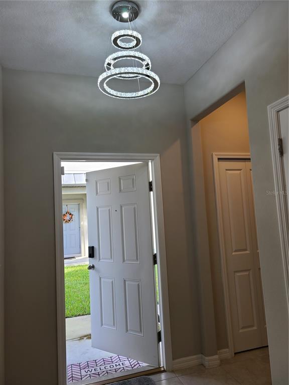 An entryway features a modern tiered crystal chandelier, a white front door, and tiled flooring — 14331 EASY GOER STREET, RUSKIN, FL