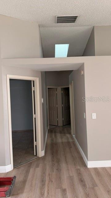 A hallway with wood-look flooring leads to multiple doorways under a vaulted ceiling with skylights — 1619 ELMSTEAD COURT, ORLANDO, FL