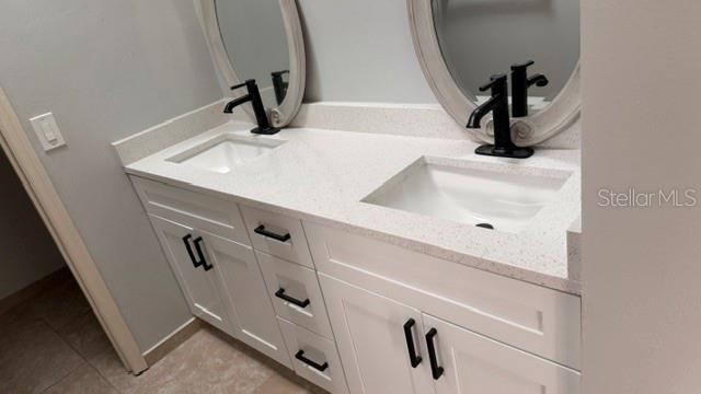 A white double-sink bathroom vanity features black faucets, oval mirrors, and a speckled stone countertop — 1619 ELMSTEAD COURT, ORLANDO, FL