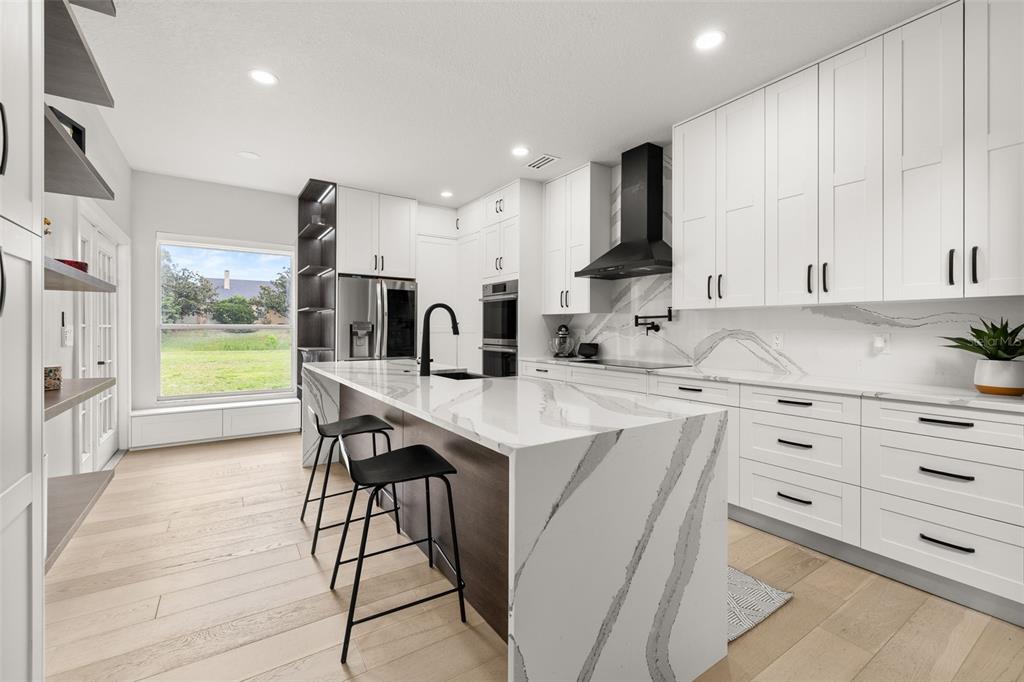 A modern kitchen features white cabinetry, a large marble-topped island, and light wood flooring — 663 CHARRICE PLACE, SANFORD, FL