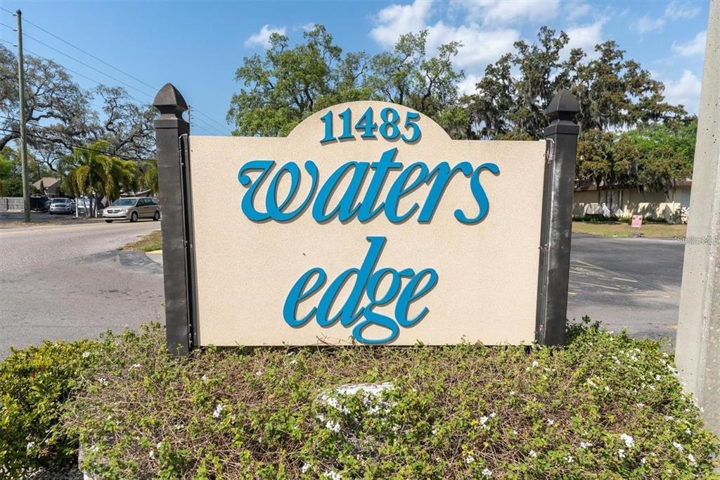 A sign for a community named Waters Edge stands in front of a landscaped area — 11485 OAKHURST ROAD UNIT 200-318, LARGO, FL