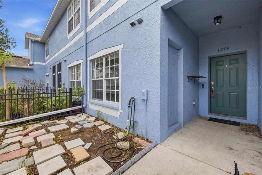 A blue stucco townhouse exterior features a green front door and a small patio area — 11009 WINTER CREST DRIVE, RIVERVIEW, FL