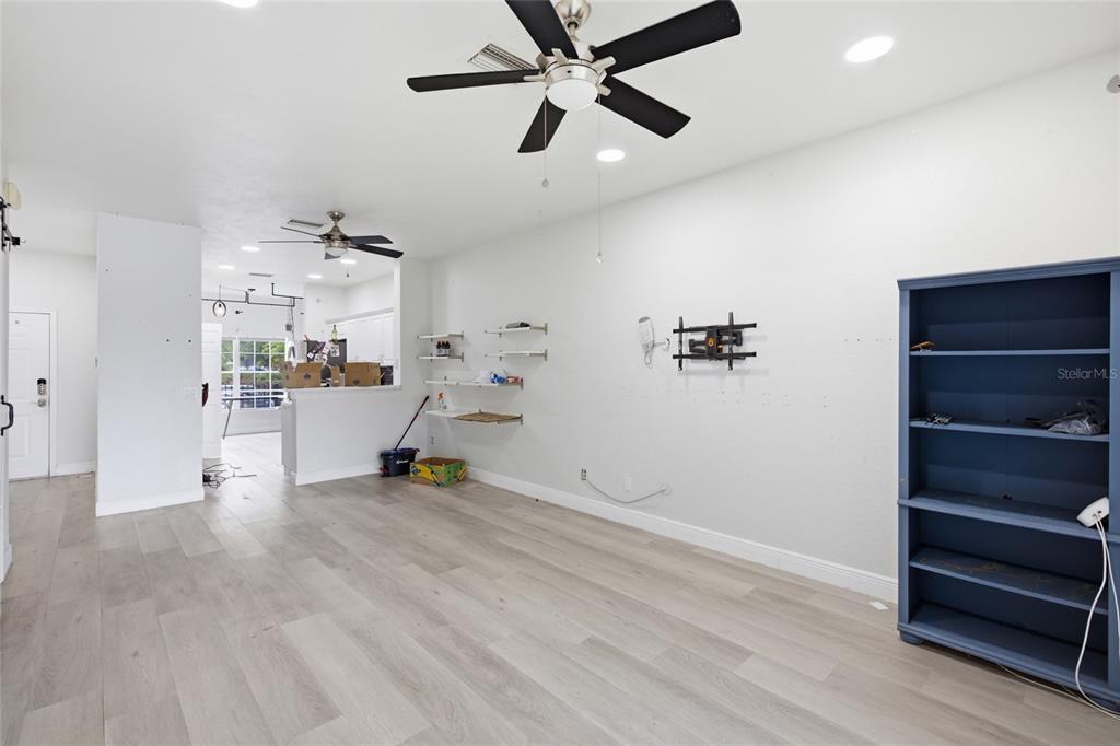 A living room with light wood-look flooring, a ceiling fan, wall shelving, and a blue bookcase — 11009 WINTER CREST DRIVE, RIVERVIEW, FL