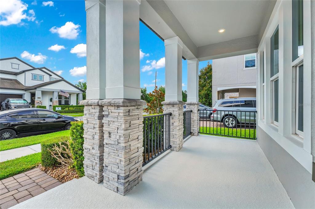 A covered front porch features stone-based columns, black metal railings, and a light-colored concrete floor — 12929 WESTSIDE VILLAGE LOOP, WINDERMERE, FL
