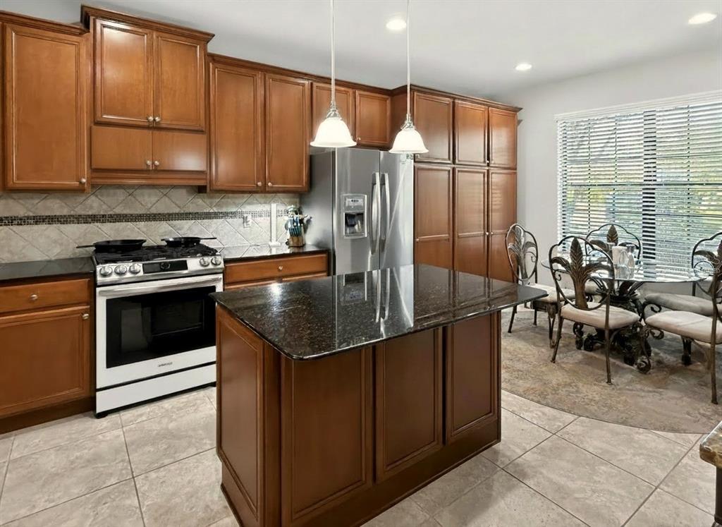 A kitchen features wood cabinets, a granite-topped island, stainless steel appliances, and a dining area — 442 DEL SOL AVE, DAVENPORT, FL