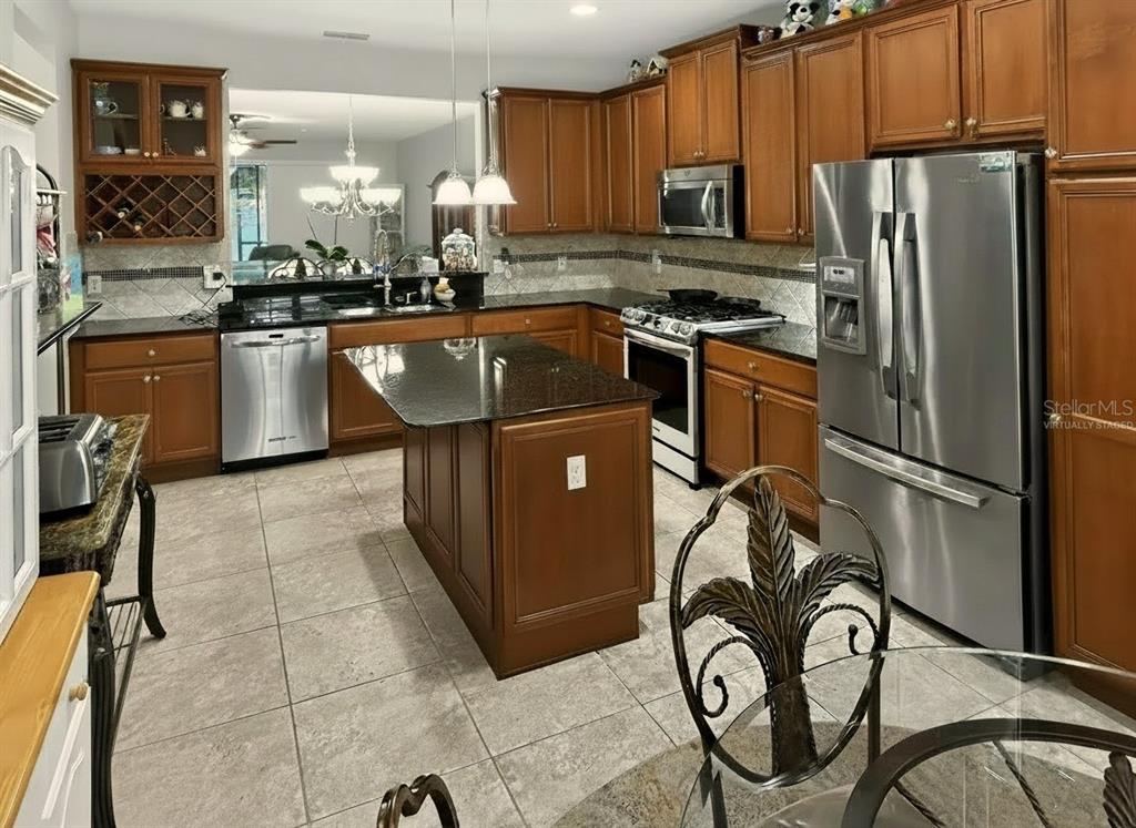 A kitchen with wood cabinets, granite countertops, a center island, and stainless steel appliances — 442 DEL SOL AVE, DAVENPORT, FL