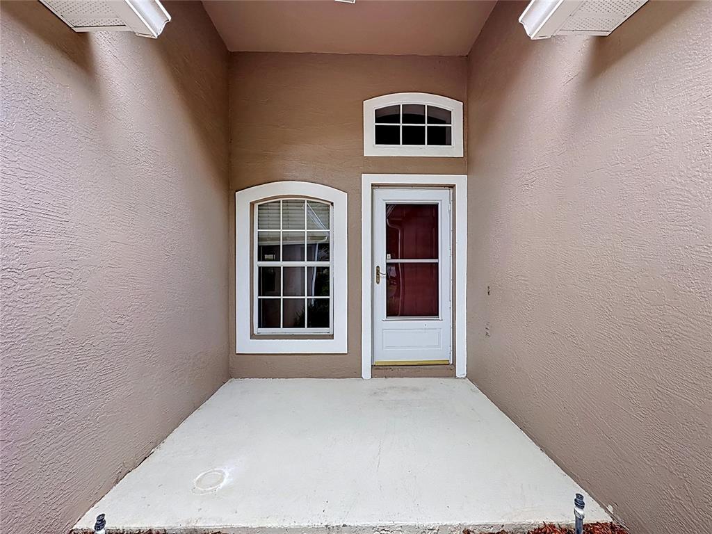 A concrete patio sits before a white front door and a window with white trim — 3675 EVERSHOLT STREET, CLERMONT, FL