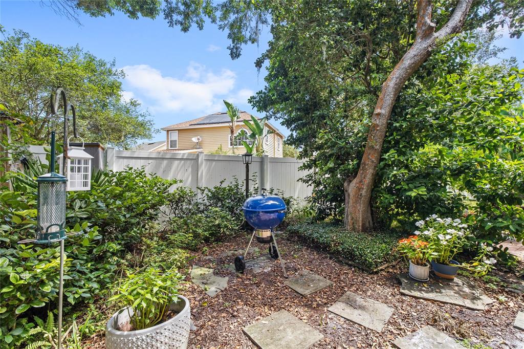 A backyard features a blue kettle grill, stone pavers, potted plants, and a white fence — 1482 CREEKSIDE CIRCLE, WINTER SPRINGS, FL