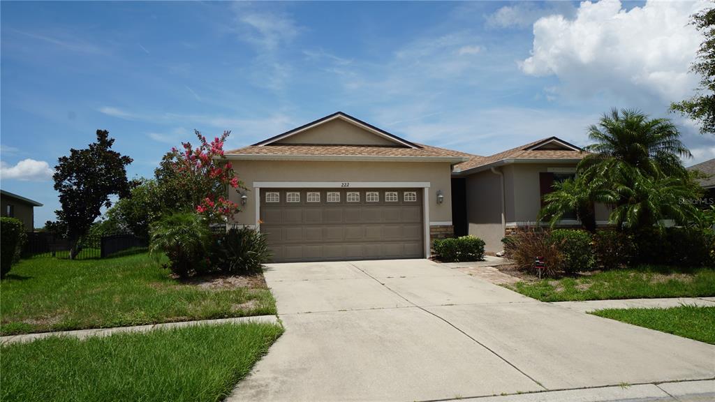 A tan single-story house features a two-car garage, a concrete driveway, and a palm tree — 222 STAR SHELL DRIVE, APOLLO BEACH, FL