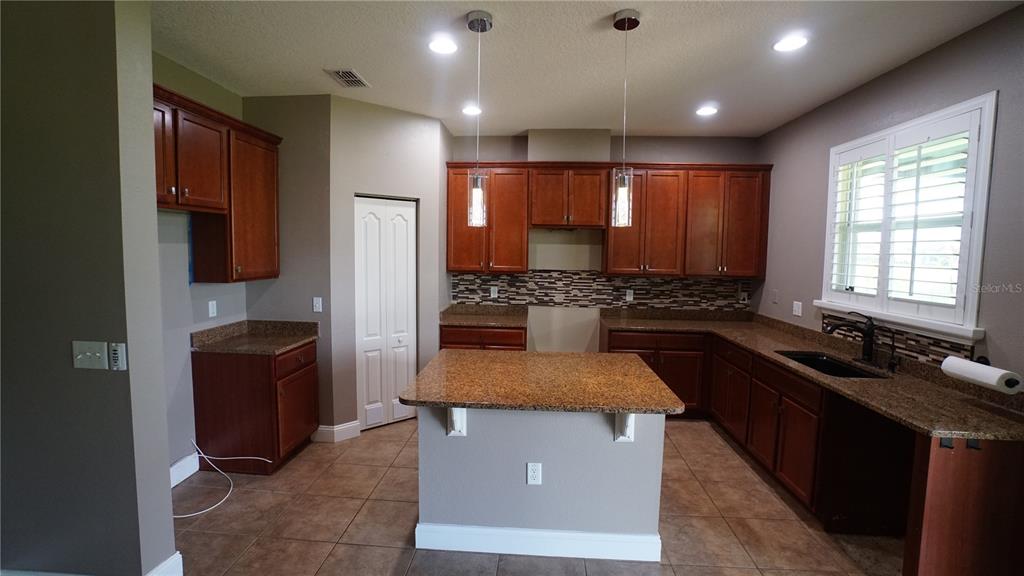 A kitchen with brown wooden cabinets, granite countertops, a center island, and tiled flooring — 222 STAR SHELL DRIVE, APOLLO BEACH, FL