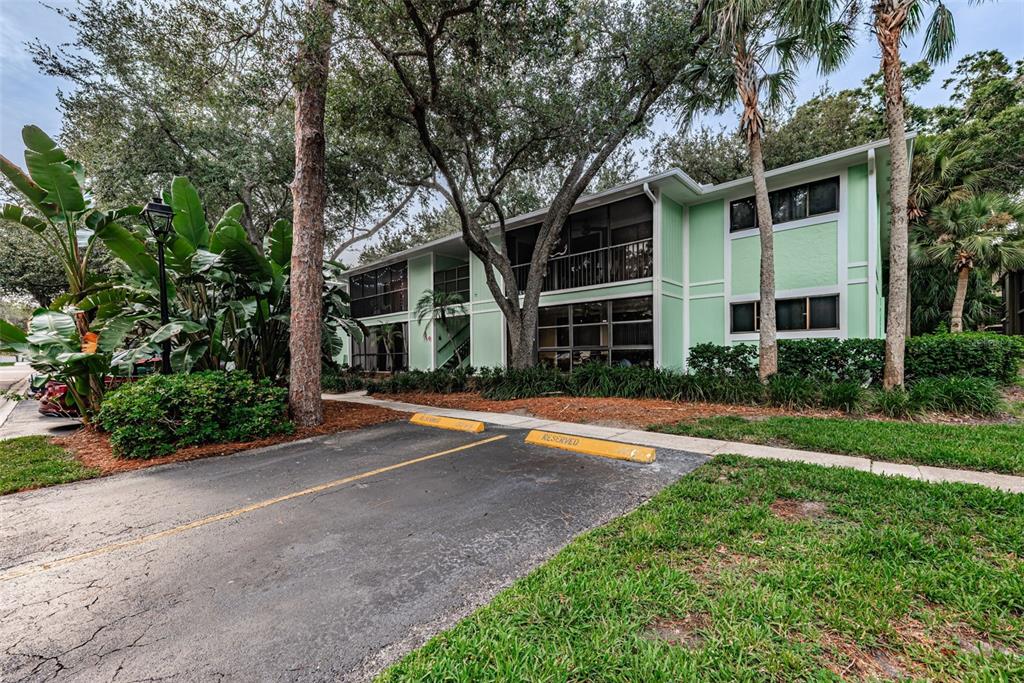 A two-story light green apartment building with screened balconies sits behind a reserved parking area — 3295 FOX CHASE CIRCLE N UNIT 107, PALM HARBOR, FL