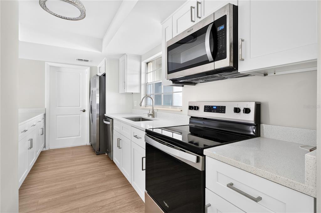 A white kitchen features stainless steel appliances, quartz countertops, and a breakfast bar — 1442 CANTERBURY CIRCLE, CASSELBERRY, FL