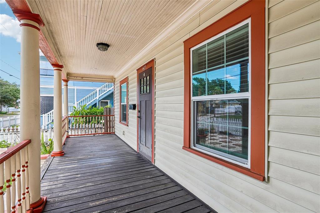 A covered wooden porch features a dark front door, white siding, and orange window trim — 467 9TH AVENUE N, ST PETERSBURG, FL