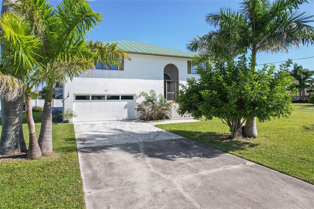 A two-story white house features a green metal roof, a garage, and palm trees — 103 TAHITI CIRCLE, NAPLES, FL