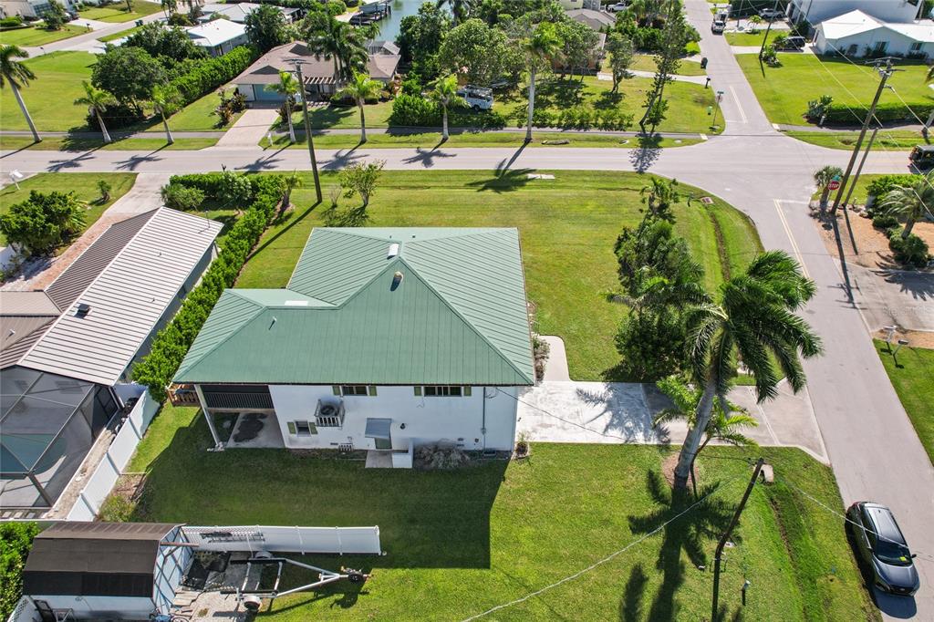 An aerial view shows a white house with a green metal roof and a large yard — 103 TAHITI CIRCLE, NAPLES, FL