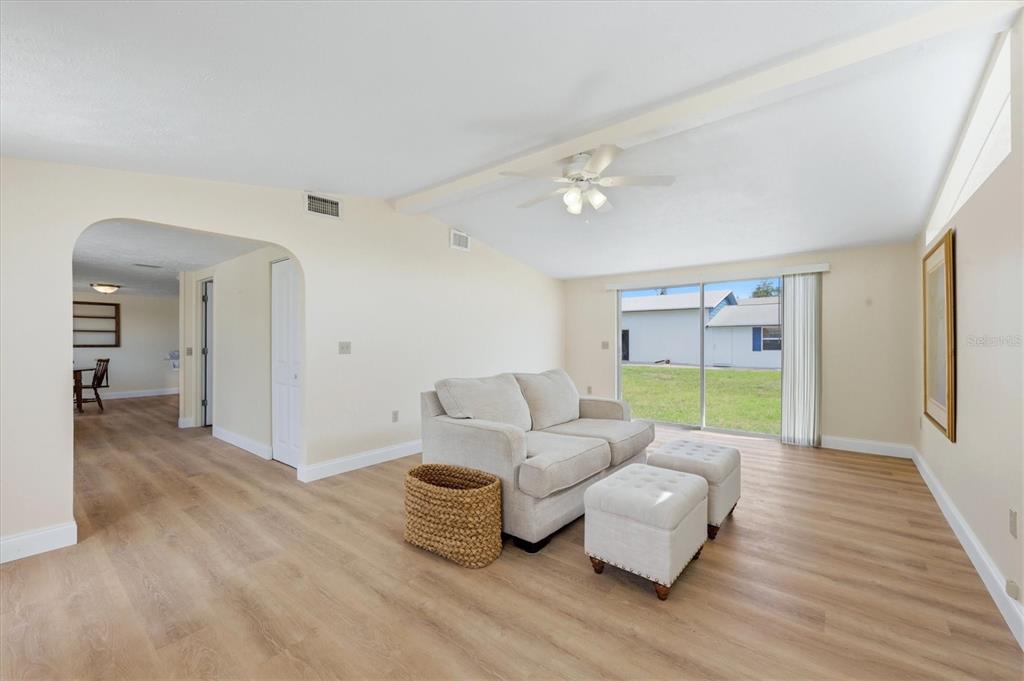 A living room features light-colored wood-look flooring, a beige sofa with ottomans, and sliding glass doors — 1157 SOUTH LANE, ENGLEWOOD, FL