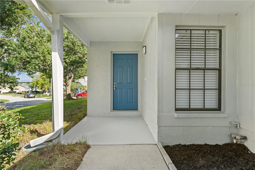 A covered concrete porch leads to a blue front door beside a window with blinds — 534 LAKE DEXTER BOULEVARD, WINTER HAVEN, FL