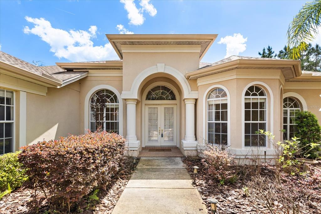 The exterior of a beige stucco house features a covered entryway with white columns — 420 VALLEY STREAM DRIVE, GENEVA, FL