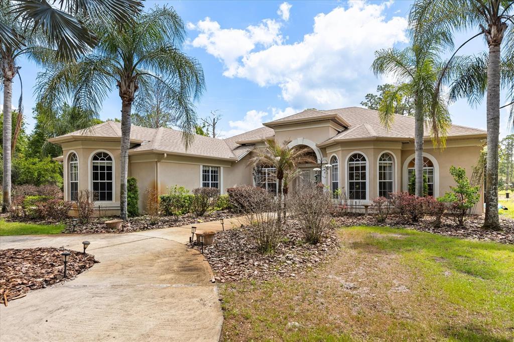 A single-story beige stucco house features a curved walkway, arched windows, and several palm trees — 420 VALLEY STREAM DRIVE, GENEVA, FL