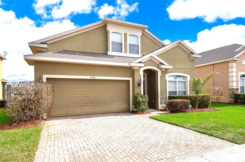 A two-story house with a tan exterior, a two-car garage, and a brick paver driveway — 1020 ANDALUSIA LOOP, DAVENPORT, FL