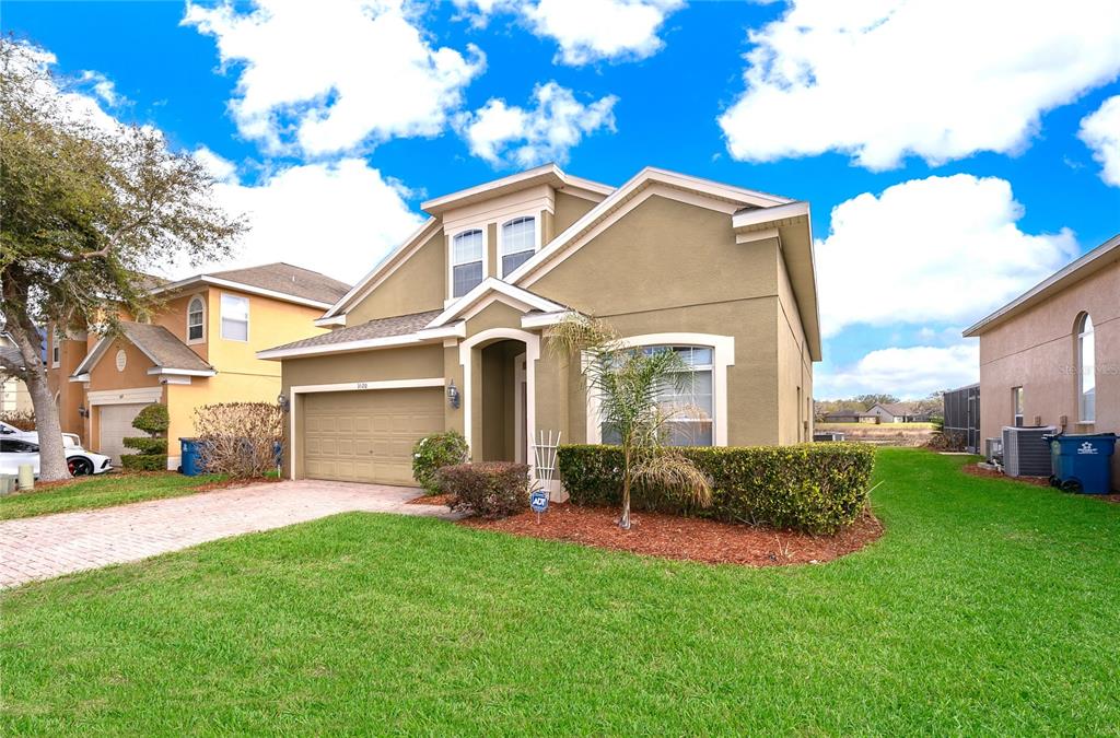 A two-story tan house with a two-car garage and a front lawn under a blue sky — 1020 ANDALUSIA LOOP, DAVENPORT, FL