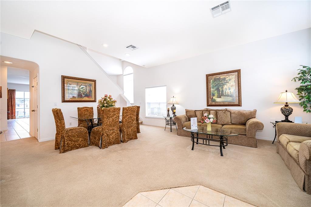 A living and dining area with beige carpet, tan furniture, and framed wall art — 1020 ANDALUSIA LOOP, DAVENPORT, FL