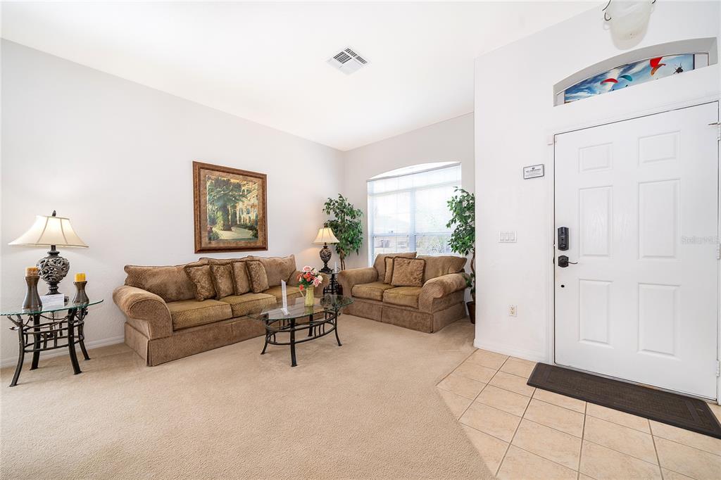 A living room with beige carpet, two brown sofas, a glass coffee table, and an entryway — 1020 ANDALUSIA LOOP, DAVENPORT, FL