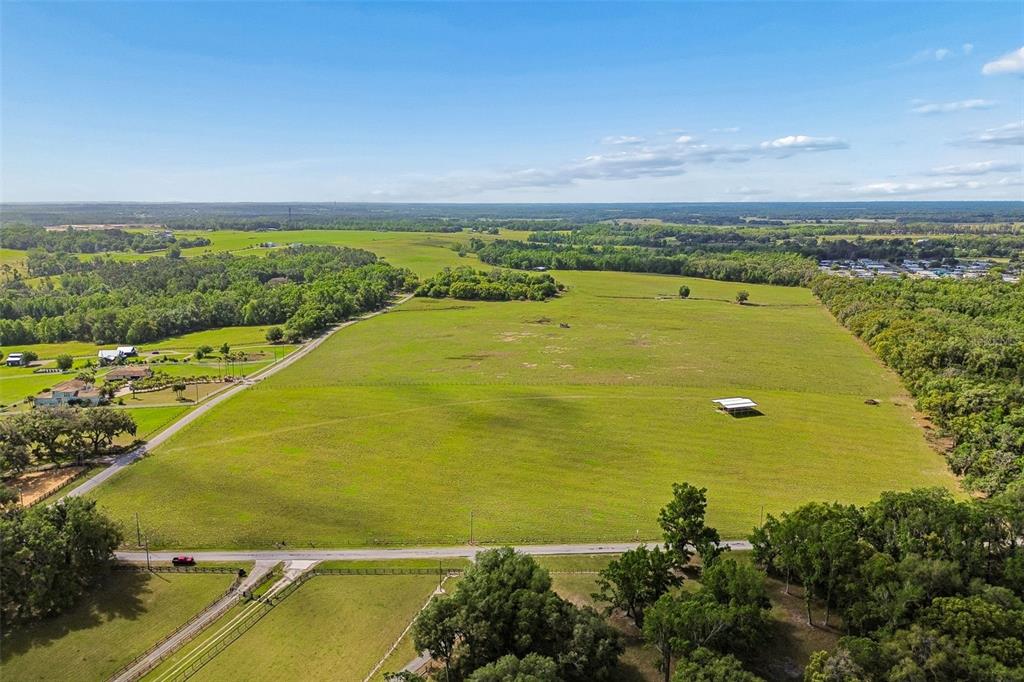 An aerial view shows a large, open green pasture bordered by trees and a road — BAYHEAD ROAD Lot 7, DADE CITY, FL