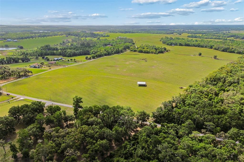 An aerial view shows a large, open green pasture bordered by trees and a road — BAYHEAD ROAD Lot 7, DADE CITY, FL